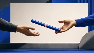 Dos manos abiertas entregándose un testigo de relevo azul cobalto con una franja ámbar, frente a un panel rectangular claro y vacío.