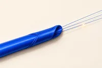 Un conducto sellado color cobalto del que se escapan tres hilos finos que continúan más allá del sello, sobre un fondo crema, con una chispa ámbar al final.
