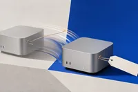 Dos cubos de escritorio plateados idénticos sobre planos cobalto y gris, con una etiqueta de precio de papel que viaja por un cordel del primero al segundo.
