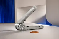 Una bisagra de aluminio abierta a medias y sin ningún panel montado encima, junto a una pequeña lámina ámbar apoyada al lado
