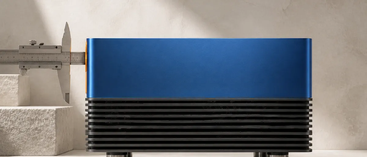 Una máquina de escritorio metálica azul cobalto con aletas de refrigeración, medida por un calibre que solo abraza una delgada lámina ámbar de su borde frontal mientras el resto del cuerpo queda sin medir.