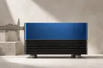 Una máquina de escritorio metálica azul cobalto con aletas de refrigeración, medida por un calibre que solo abraza una delgada lámina ámbar de su borde frontal mientras el resto del cuerpo queda sin medir.