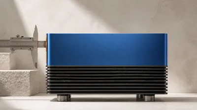 Una máquina de escritorio metálica azul cobalto con aletas de refrigeración, medida por un calibre que solo abraza una delgada lámina ámbar de su borde frontal mientras el resto del cuerpo queda sin medir.